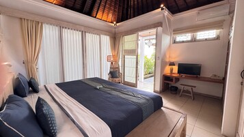Quarto com cama, cortinas, escrivaninha com televisão e cadeira.