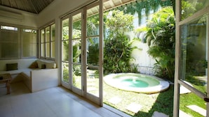 A modern interior with large glass doors leading to a lush garden and a hot tub. - Artemis Villa and Hotel (Seminyak)