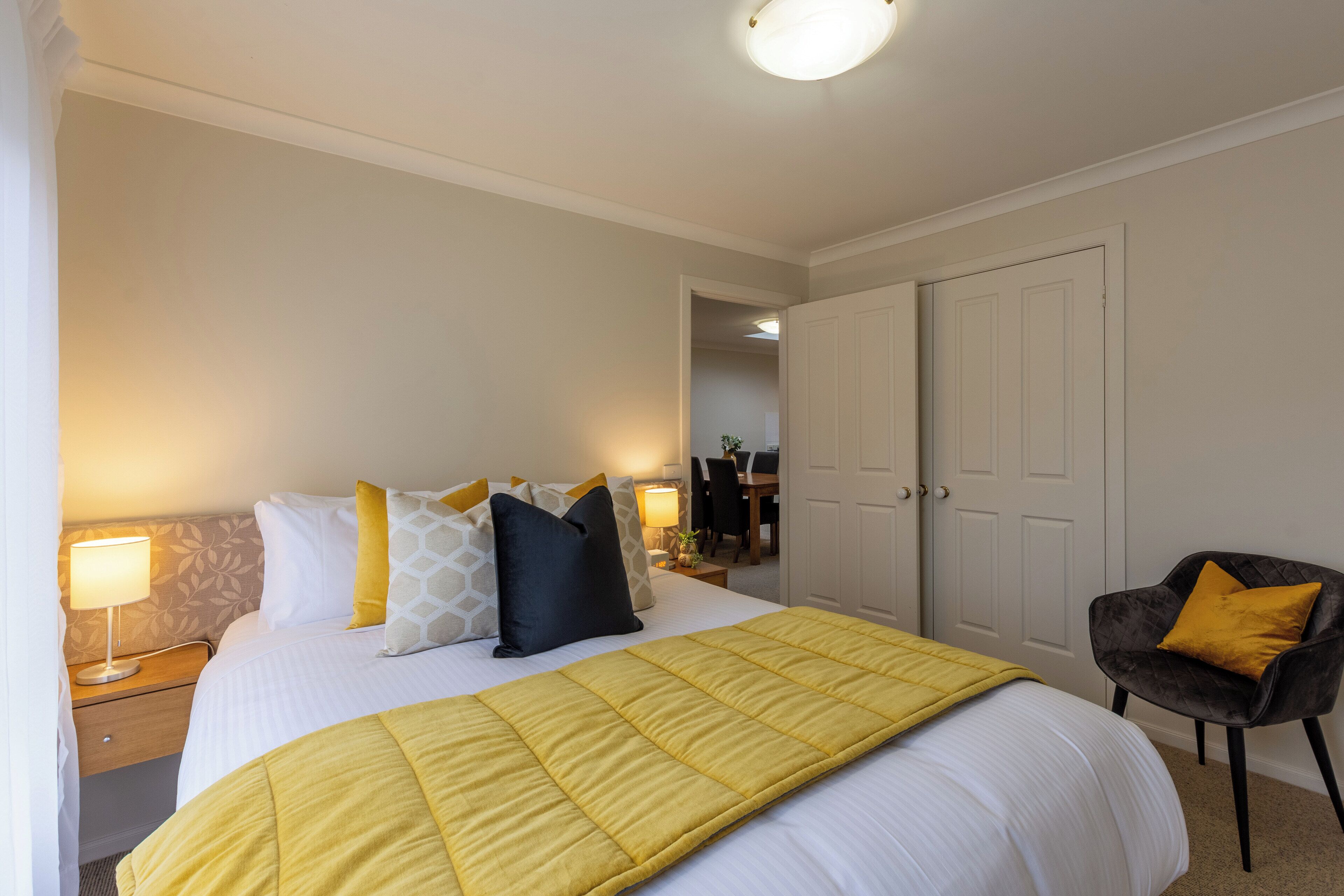 A hotel room with a bed, bedside tables, a chair, and a door.