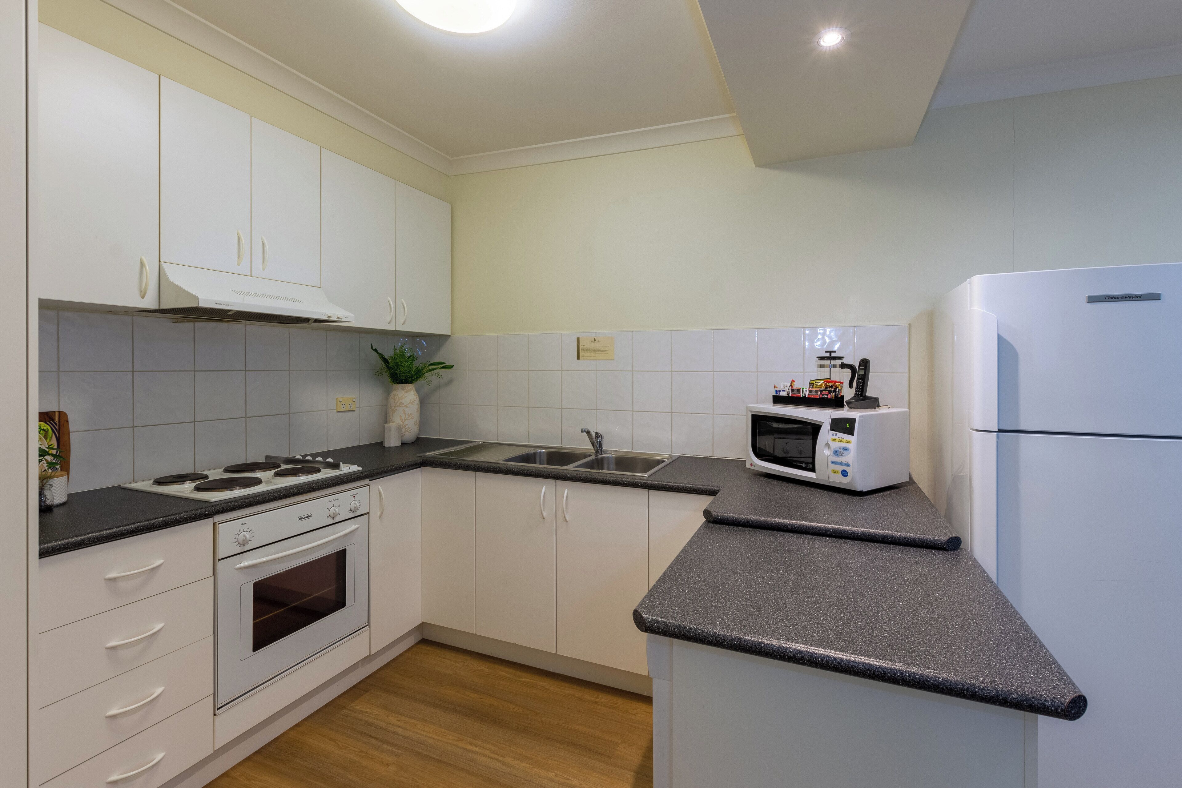 A modern kitchen with white cabinets, a built-in oven, a microwave, and a refrigerator.