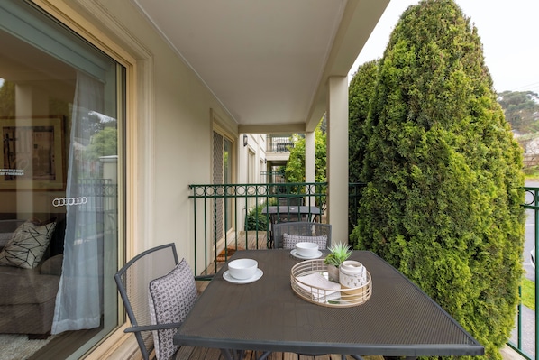 A balcony with a table set for dining, a sofa, and a tall green hedge.