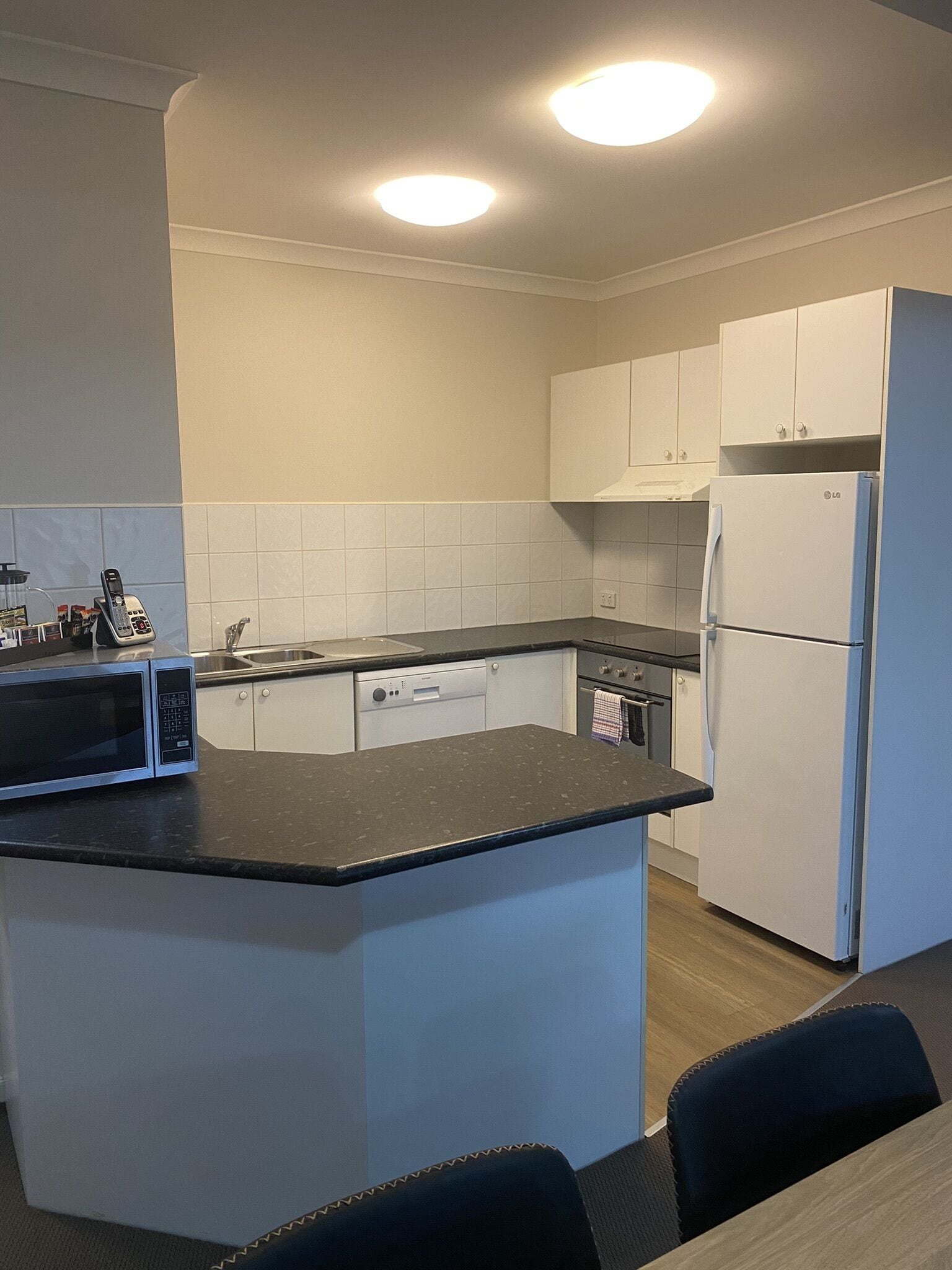 A compact kitchen with white cabinets, a black countertop, a microwave, a refrigerator, and a sink.