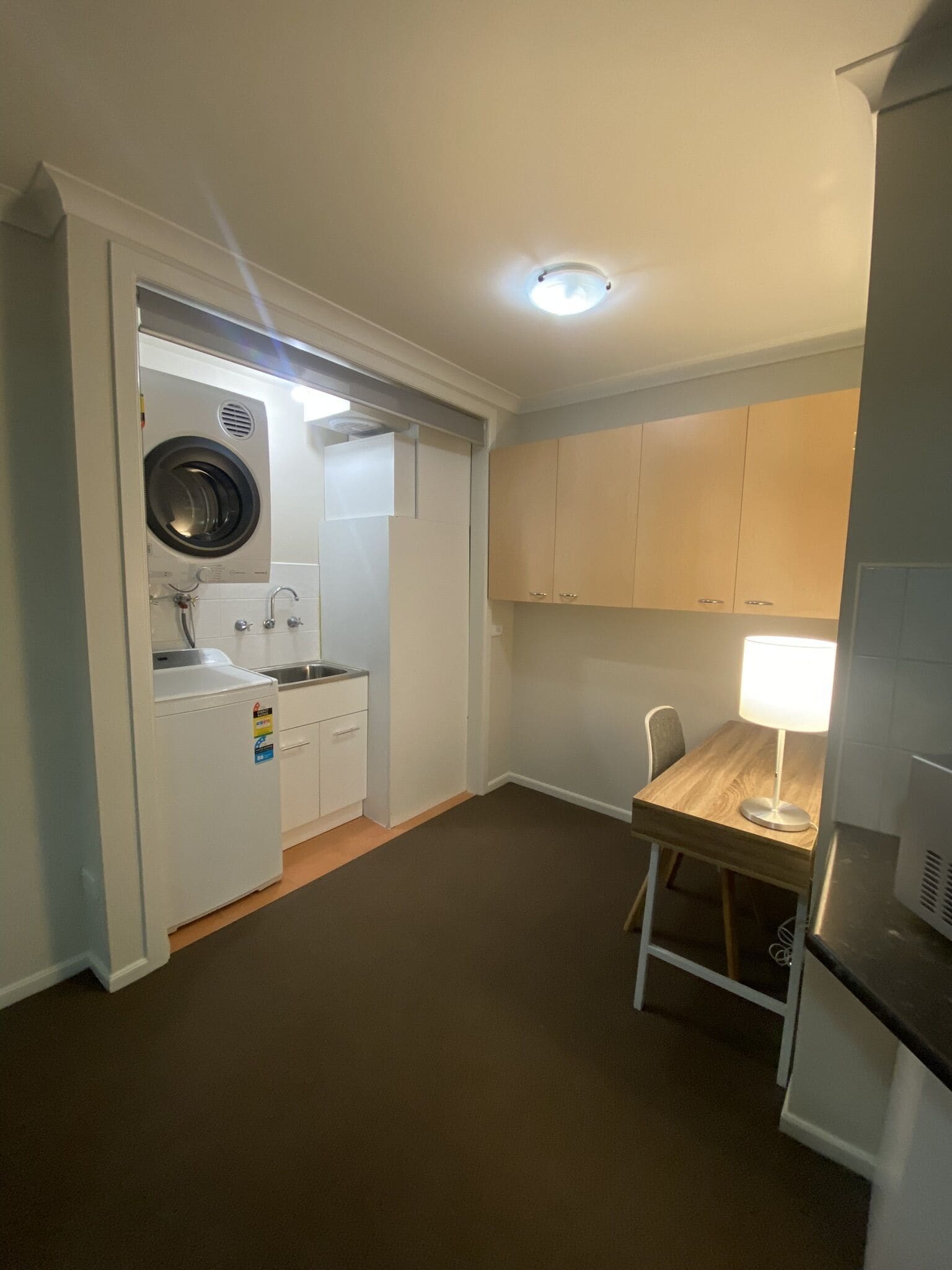 A compact kitchen with a built-in washer and dryer, a small dining table with a lamp, and wooden cabinets.