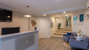 Een moderne woonkamer met een grijze bank, een flatscreen-tv, een houten vloer en een trap naar een hoger niveau.