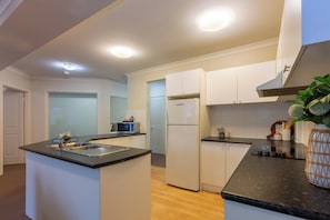 A modern kitchen with white cabinets, a black countertop, a built-in microwave, and a refrigerator.