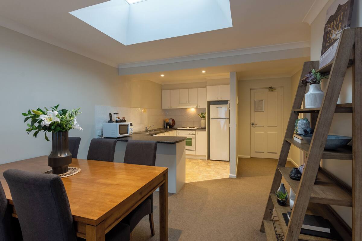A modern kitchen with white cabinets, a central island, and a skylight above the dining area.