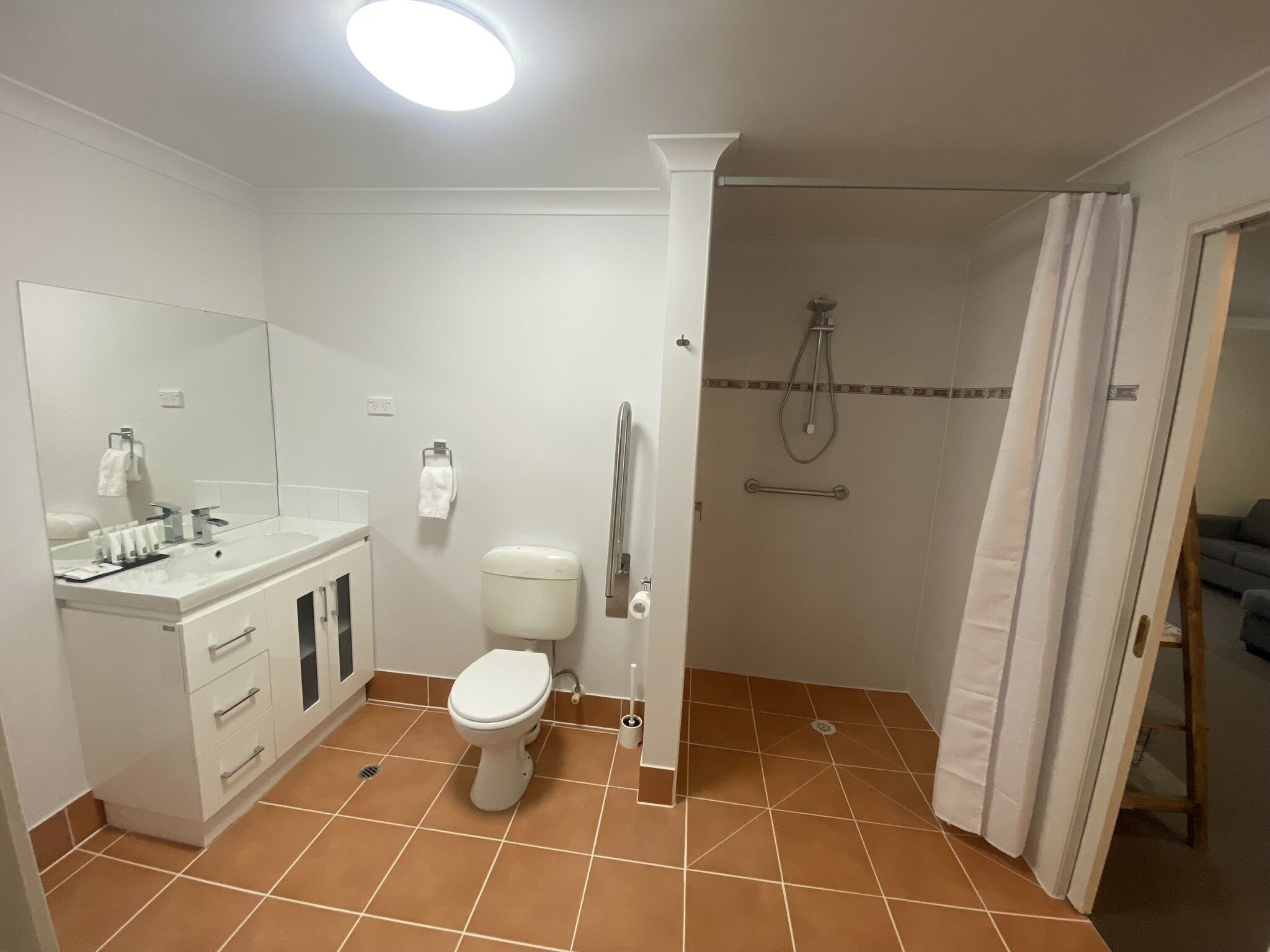 Ein Badezimmer mit Toilette, Waschbecken mit Spiegel und Duschbereich mit Haltestange.