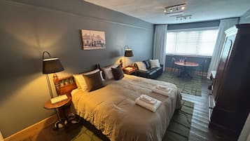 Une chambre d’hôtel avec un lit, des lampes de chevet, une petite table, un canapé, une table à manger et une fenêtre avec des rideaux.