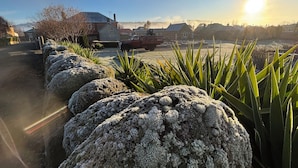 Paisaje rural con un muro de piedra, una camioneta estacionada y casas al fondo.
