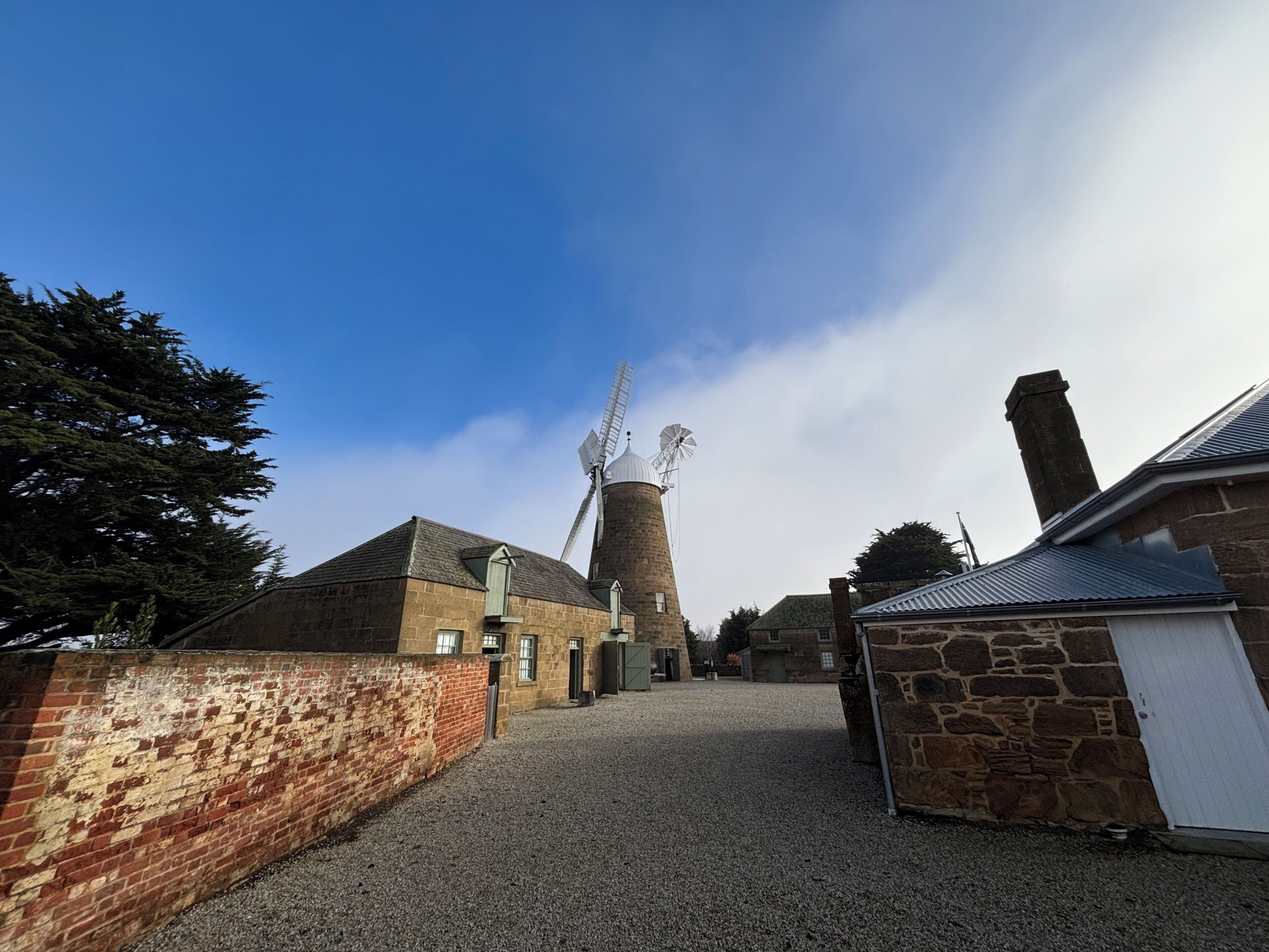 A stone windmill with a gravel path leading to a brick building.