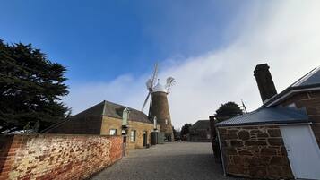 A stone windmill with a gravel path leading to a brick building.