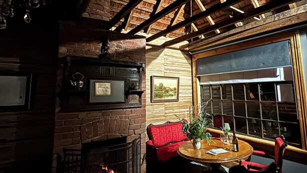 Una habitación acogedora con chimenea, vigas de madera, una mesa redonda y asientos cómodos.