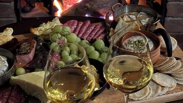 A charcuterie board with various meats, cheeses, and grapes, accompanied by glasses of white wine, set against a backdrop of a fireplace with flames.