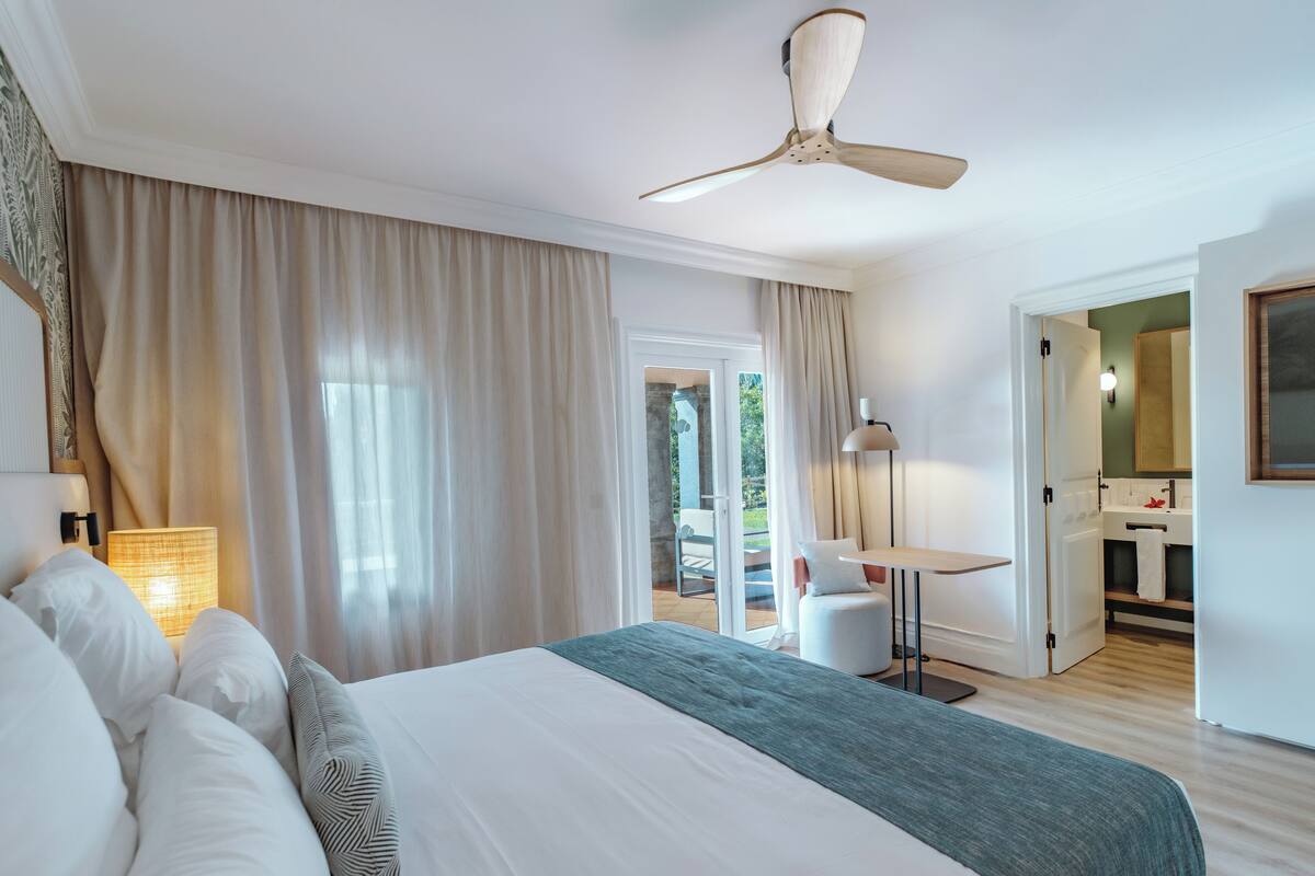 A hotel room with a large bed, a ceiling fan, a desk, and a bathroom visible through an open door.