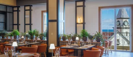 Un ristorante con diversi tavoli, sedie arancioni e piante in vaso.