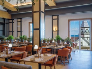 A restaurant with multiple tables, orange chairs, and potted plants. - Hyatt Ziva Madeira (Machico)