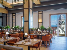 A restaurant with multiple tables, orange chairs, and potted plants.
