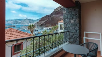 Un balcón con vista a un puerto deportivo, paredes de piedra y una mesa con sillas.