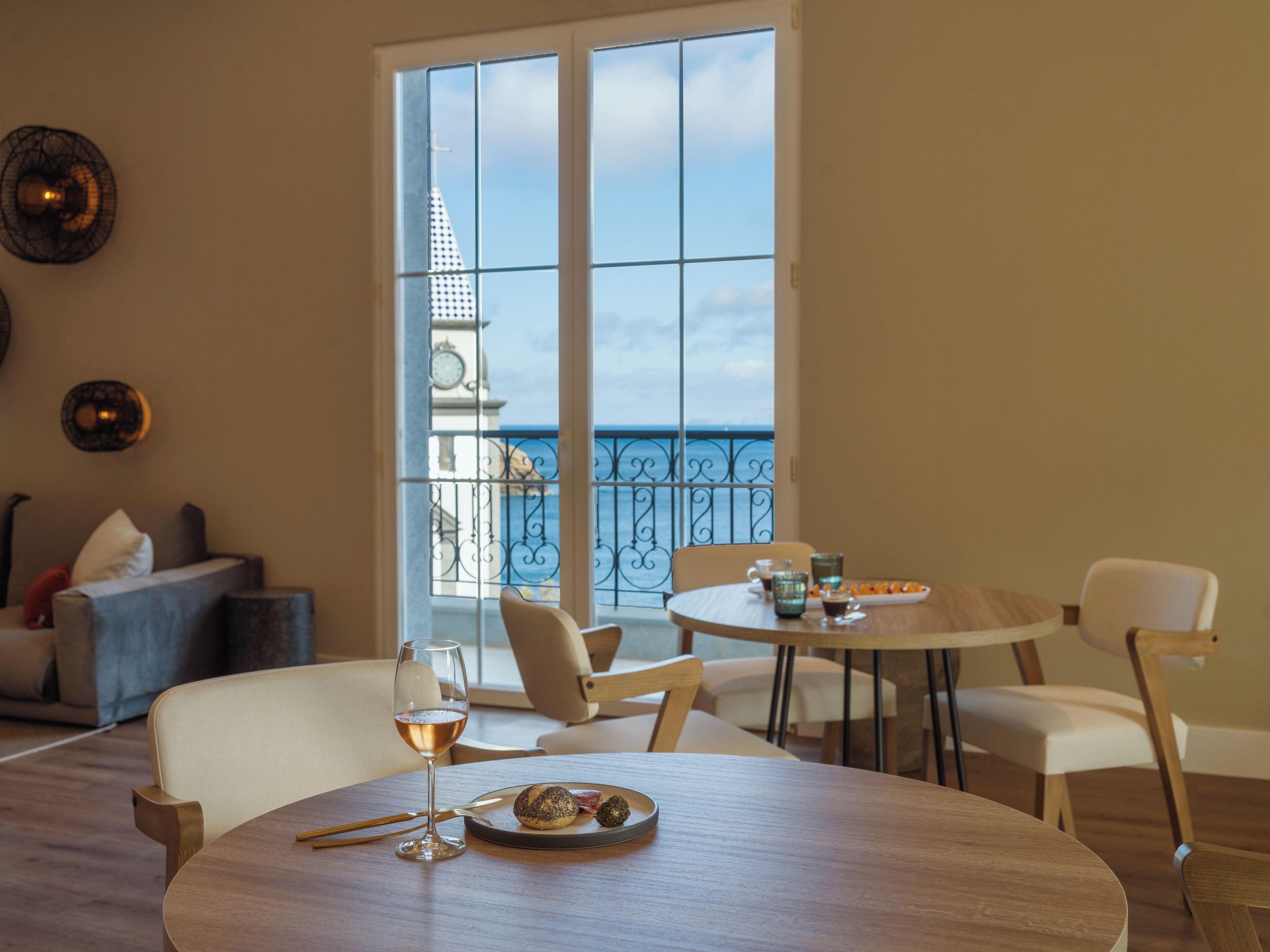 Un comedor con una mesa preparada para dos personas, una copa de vino y un plato de comida. La habitación tiene vistas al mar a través de amplios ventanales.
