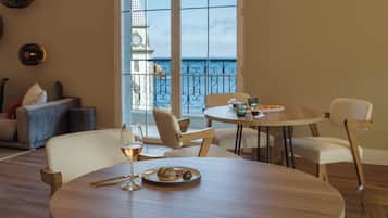 Un comedor con una mesa preparada para dos personas, una copa de vino y un plato de comida. La habitación tiene vistas al mar a través de amplios ventanales.