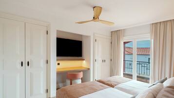 A hotel room with a bed, a desk, a ceiling fan, a TV, and a window with a view of buildings.