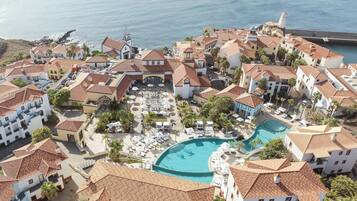 A coastal resort with multiple buildings, a central swimming pool, and a view of the sea.