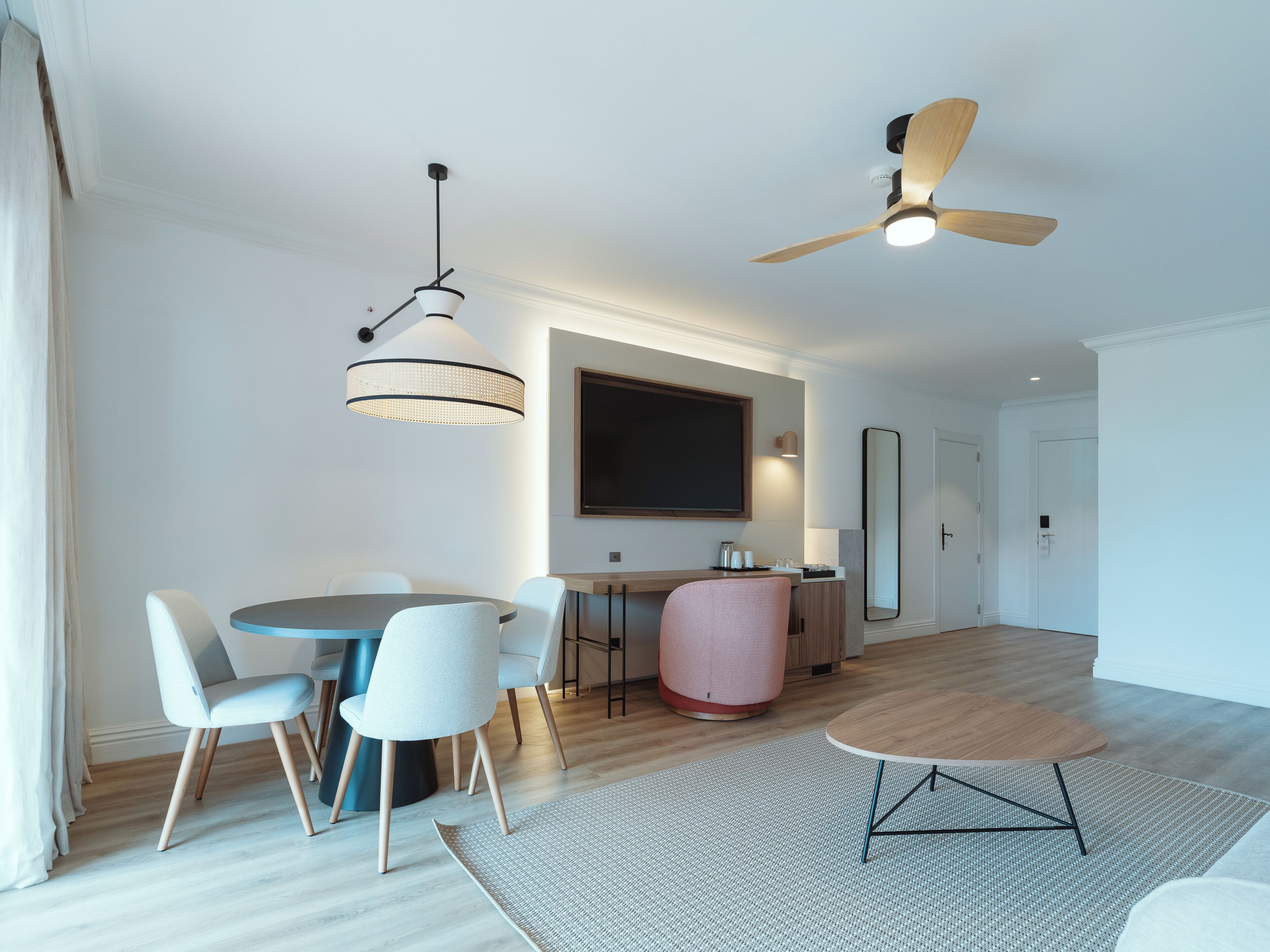 A modern living room with a dining area, a ceiling fan, and a large flat-screen TV.