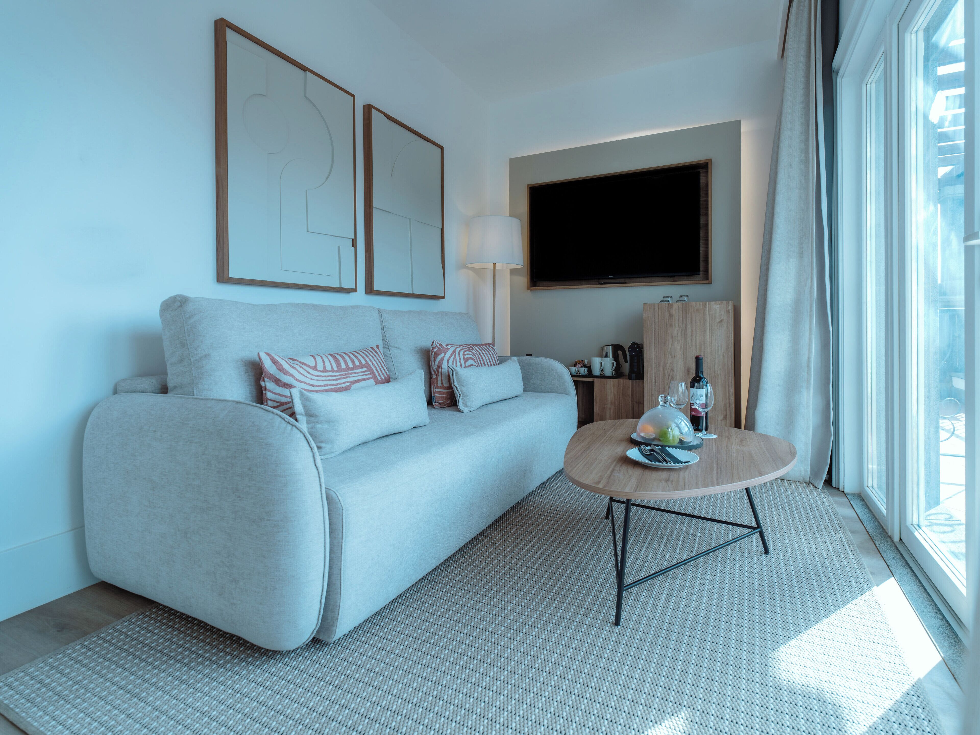 A modern living room with a sofa, a coffee table, a flat-screen TV, and a window with curtains.
