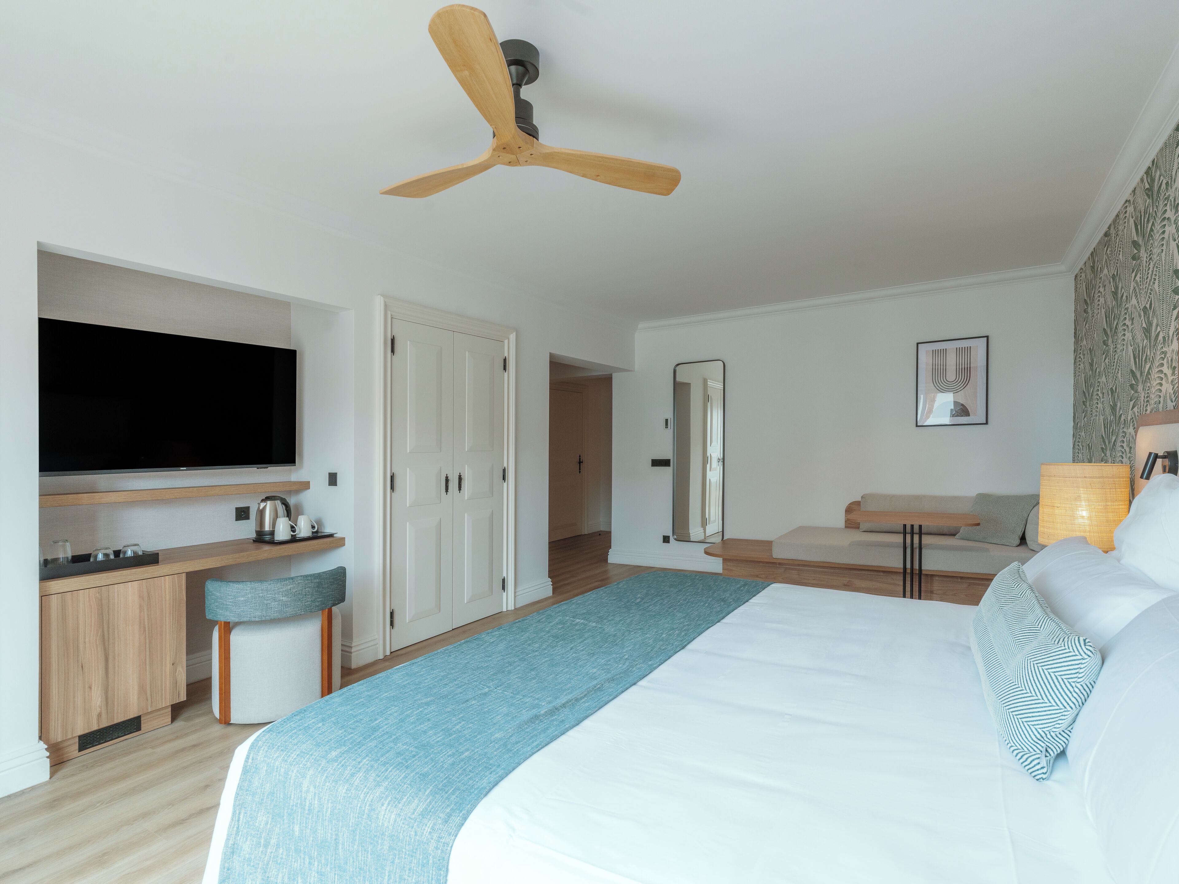 Une chambre d’hôtel moderne dotée d’un grand lit, d’un bureau avec un téléviseur à écran plat, d’un ventilateur de plafond et d’un miroir.
