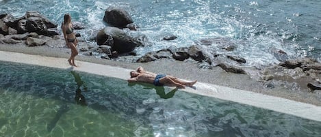 A pool with clear water, a sandy bottom, and rocks along the edge.