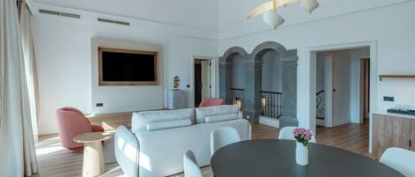 A modern living room with a grey sofa, a round dining table, and a TV mounted on the wall.