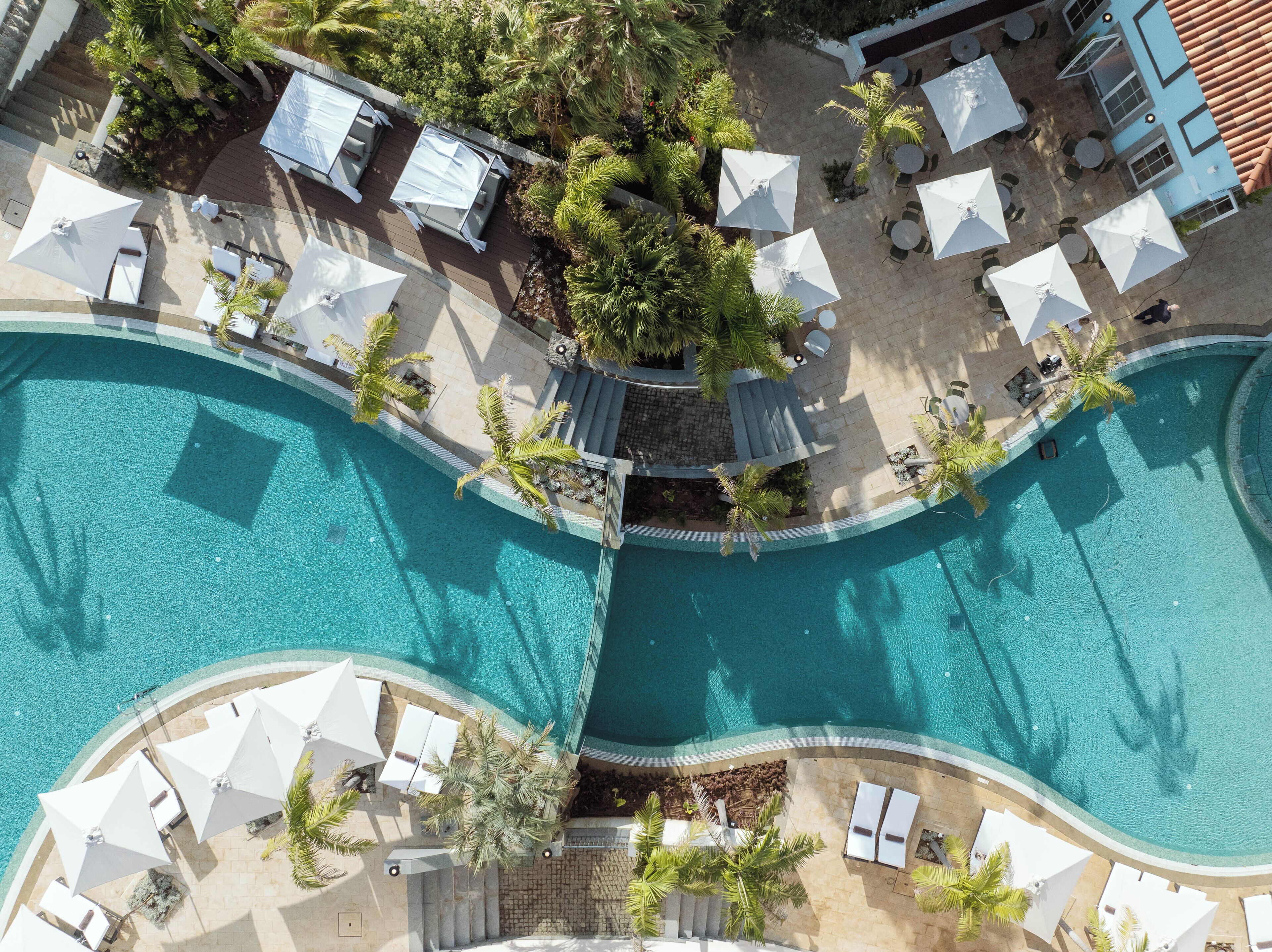 A large, curved swimming pool with white umbrellas and lounge chairs around it.