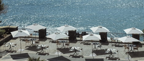 Una terraza al aire libre con mesas, sillas, sombrillas y vistas al mar.