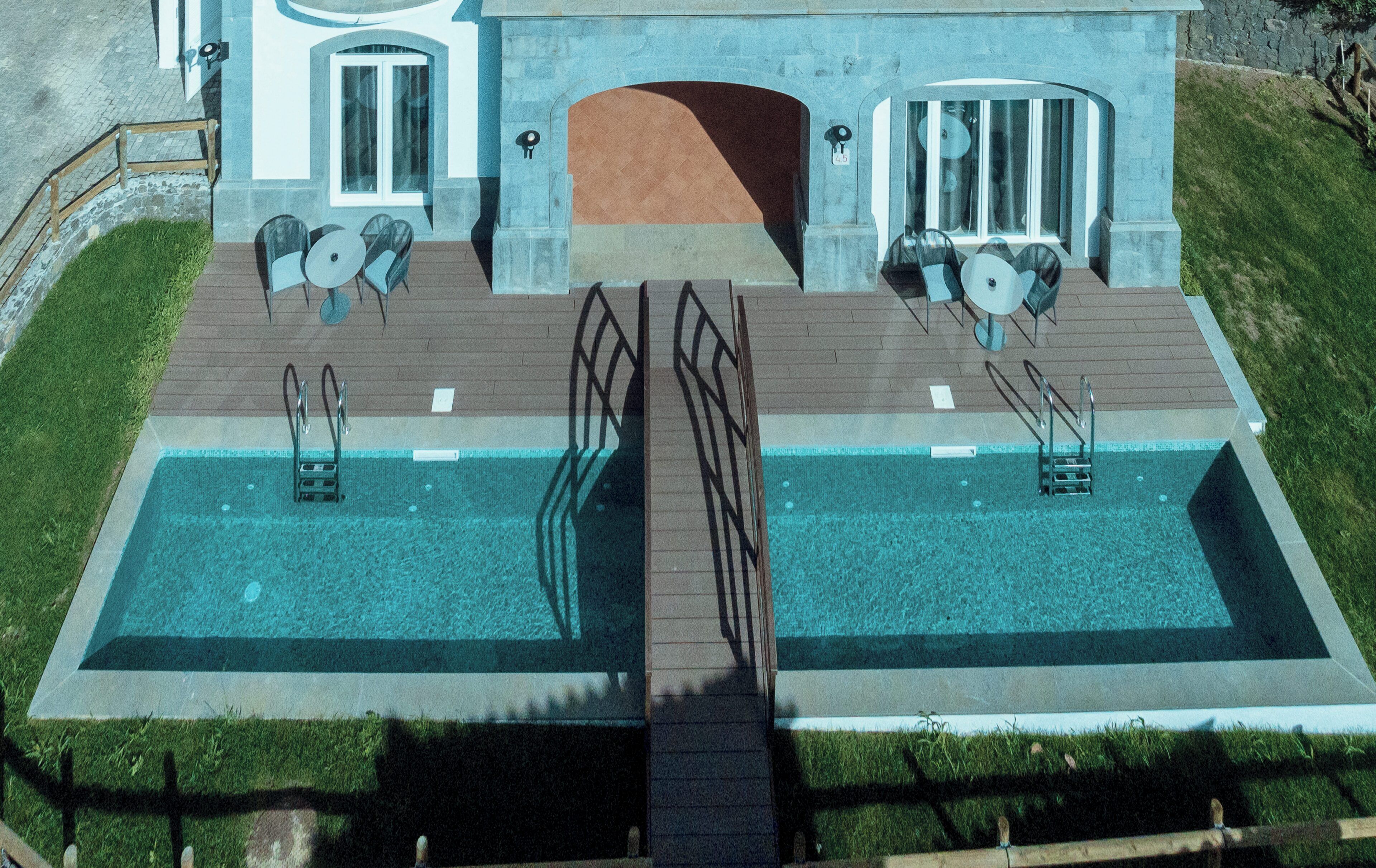 Ein großer Swimmingpool mit einer Brücke, Sitzgelegenheiten im Freien und einer Steinfassade.