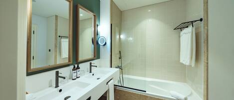 A modern bathroom with a double sink vanity, a large mirror, a handheld showerhead, and a bathtub.