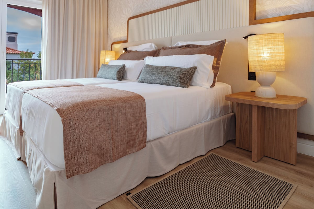 A hotel room with a large bed, a nightstand with a lamp, and a view of the outside.