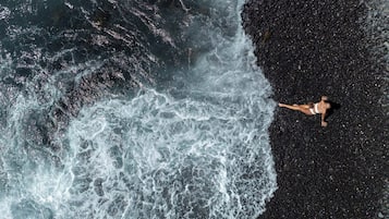 Une personne allongée sur une plage de sable noir, avec des vagues qui déferlent à proximité.
