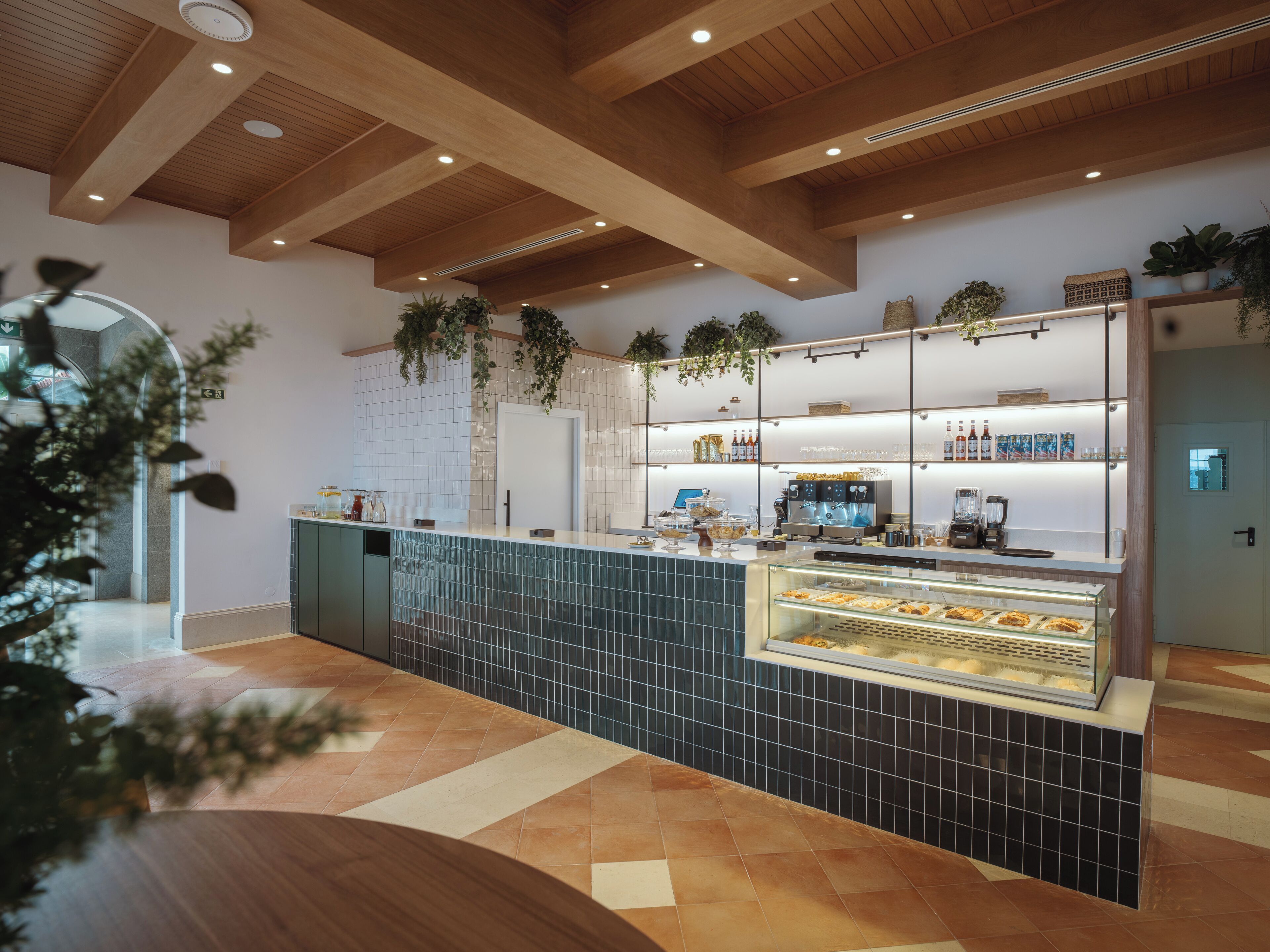 Un café moderne avec un plafond en bois, un sol carrelé et un comptoir où sont exposées des pâtisseries.