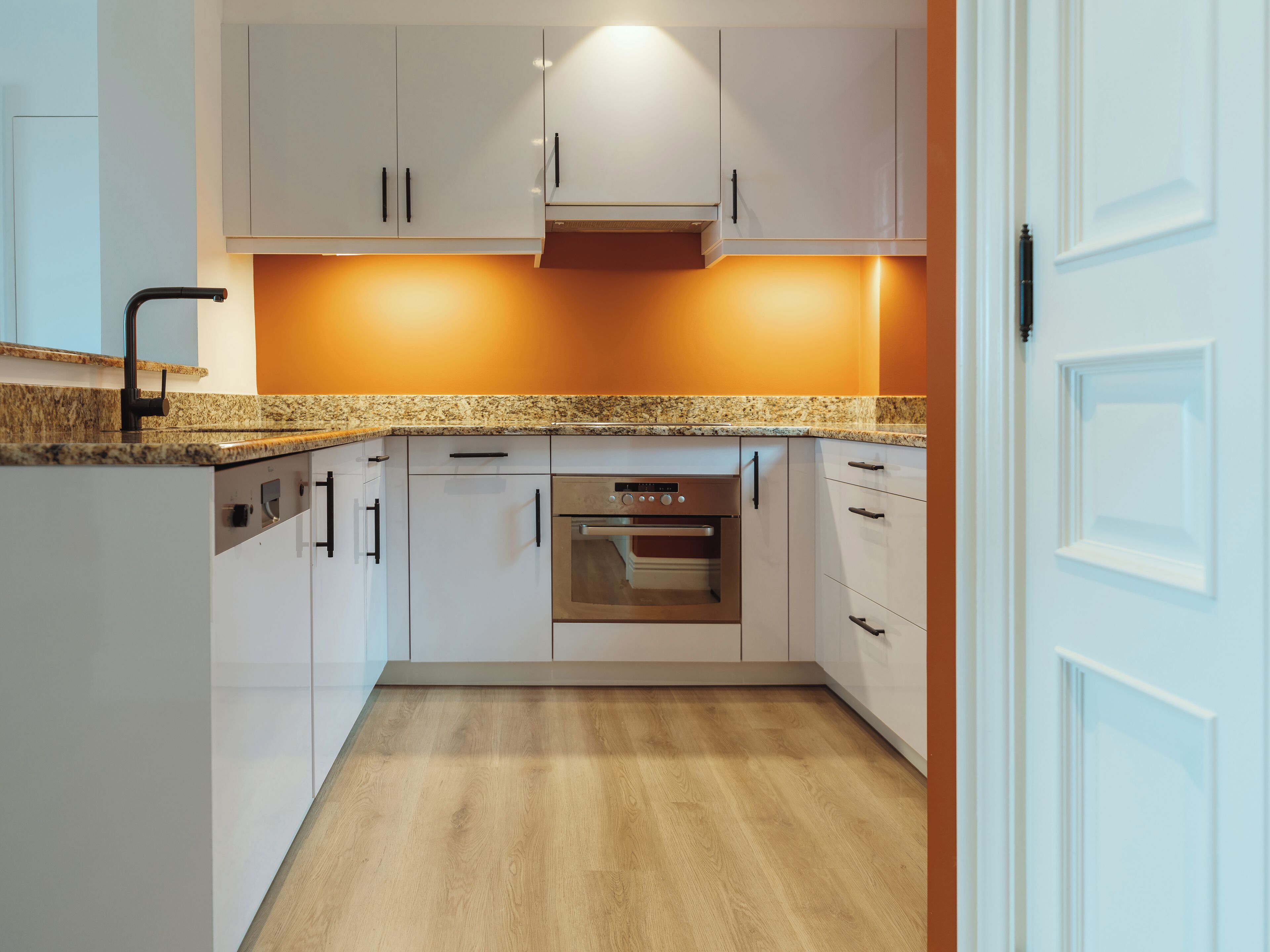 A modern kitchen with white cabinets, a built-in oven, and a granite countertop.