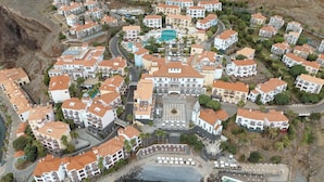 An aerial view of a coastal resort with multiple buildings, a central pool, and a rocky shoreline. - Hyatt Ziva Madeira (Machico)