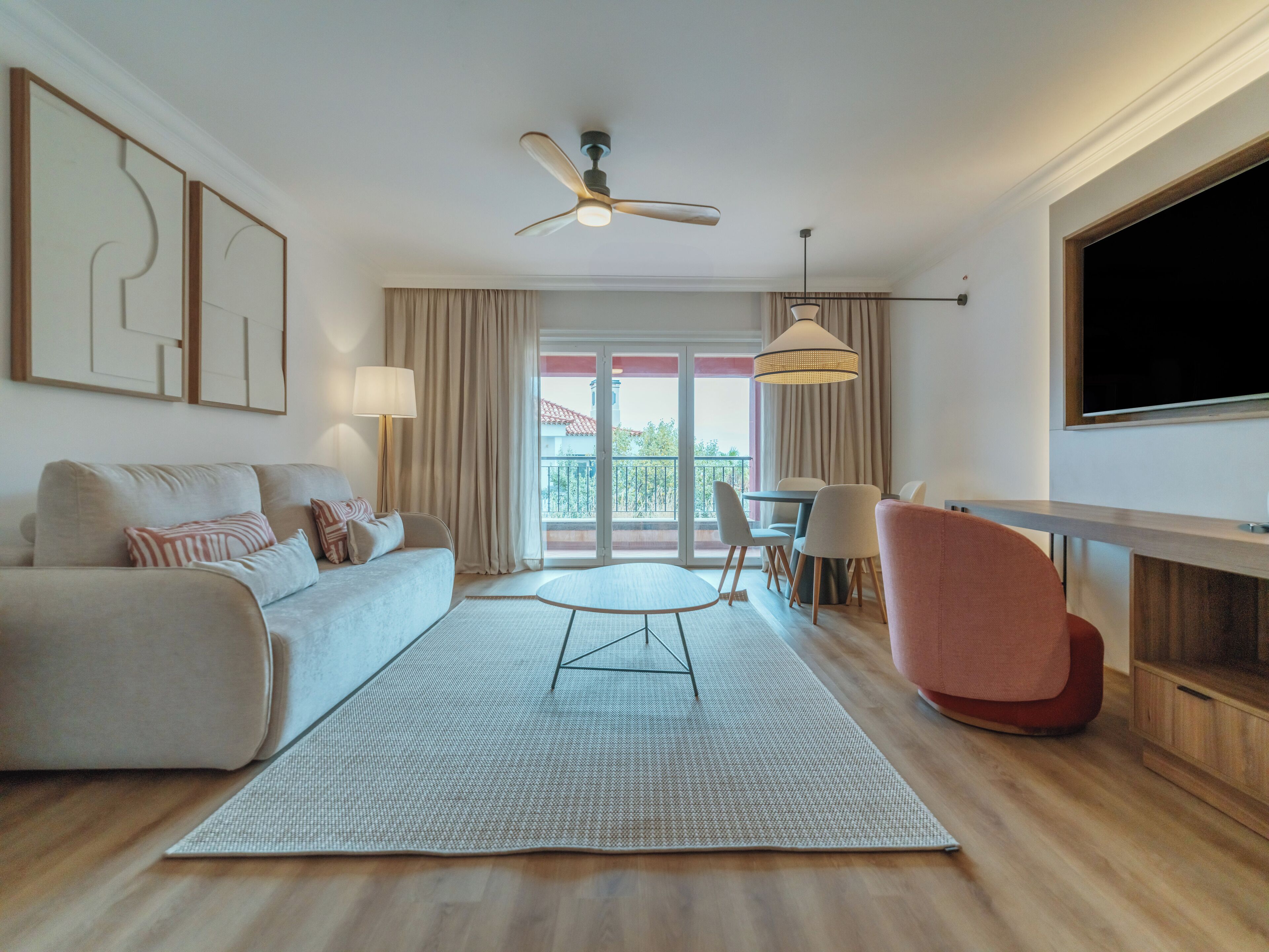 A modern living room with a sofa, a coffee table, a TV, and a balcony with curtains.