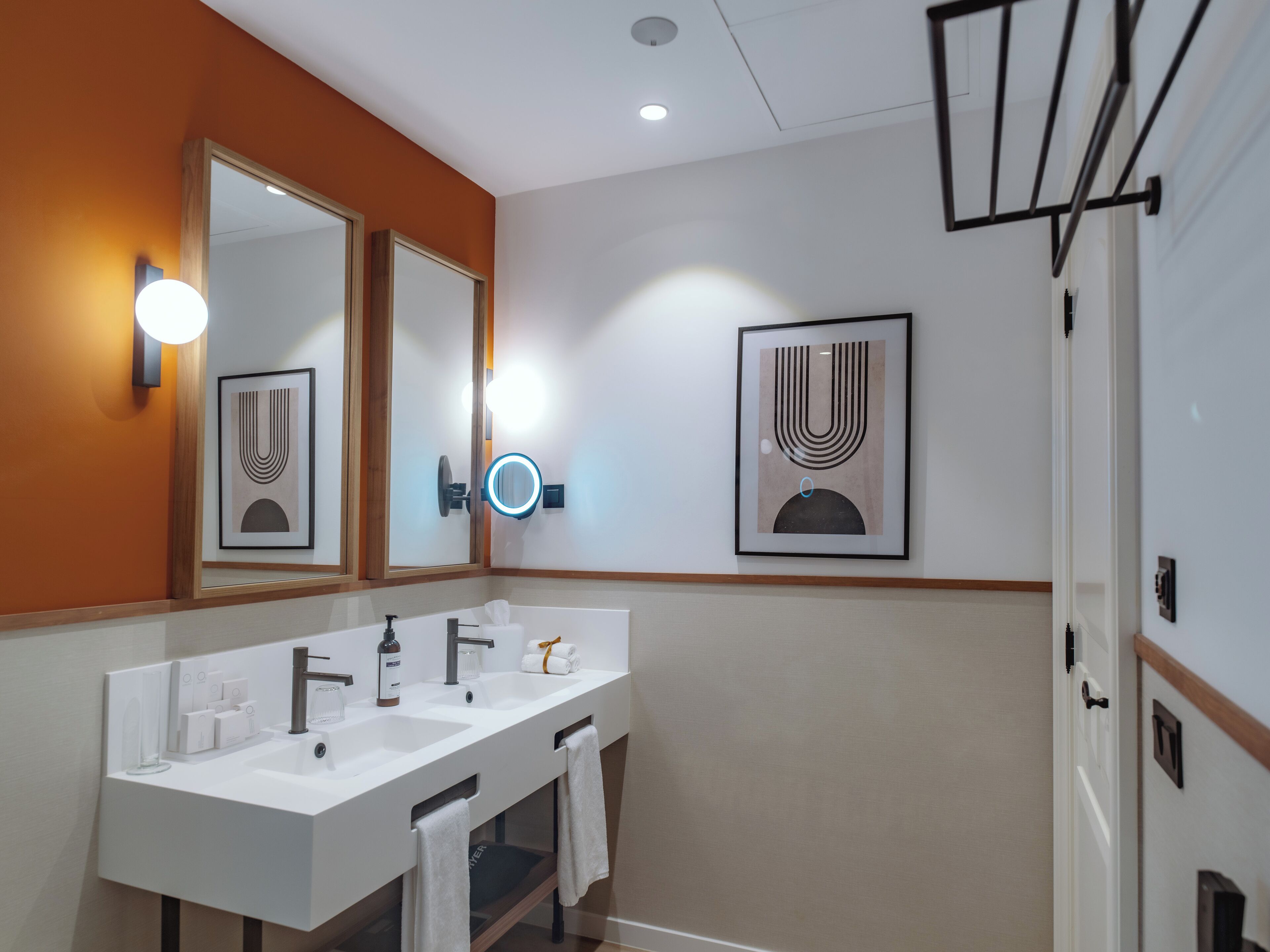 Un baño moderno con un lavamanos blanco, dos espejos y obras de arte enmarcadas en la pared.