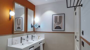 Un baño moderno con un lavamanos blanco, dos espejos y obras de arte enmarcadas en la pared.