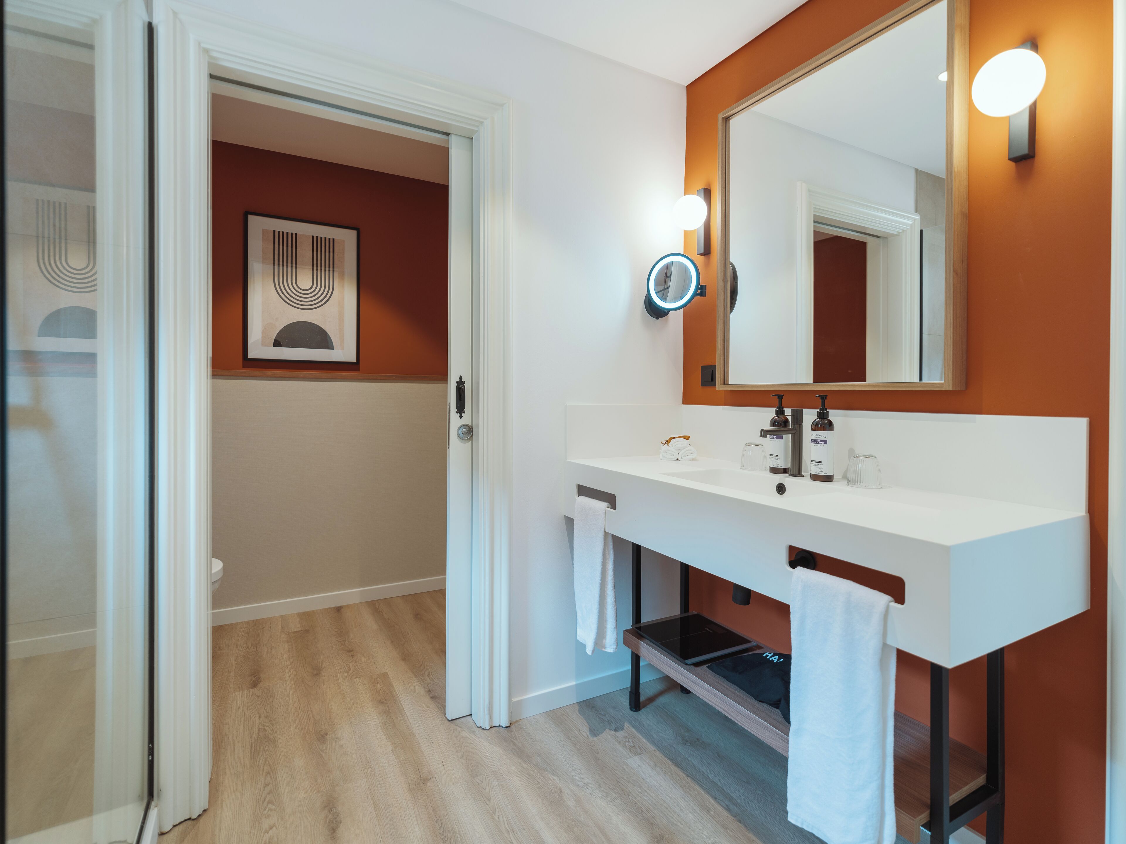 Un baño moderno con un tocador blanco, un espejo grande y piso de madera.