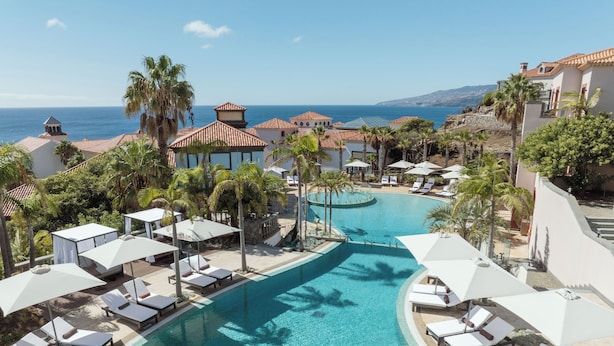 A resort pool area with clear blue water, sun loungers, umbrellas, and a view of the sea. - Hyatt Ziva Madeira (Machico)