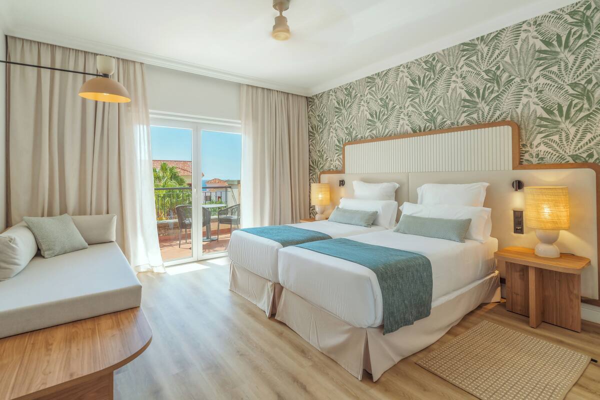 A hotel room with two beds, a sofa, a balcony, and a view of the outdoors.
