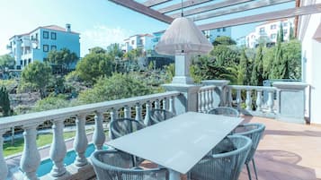 Terraza al aire libre con mesa y sillas, una lámpara colgante y vistas a edificios y vegetación.