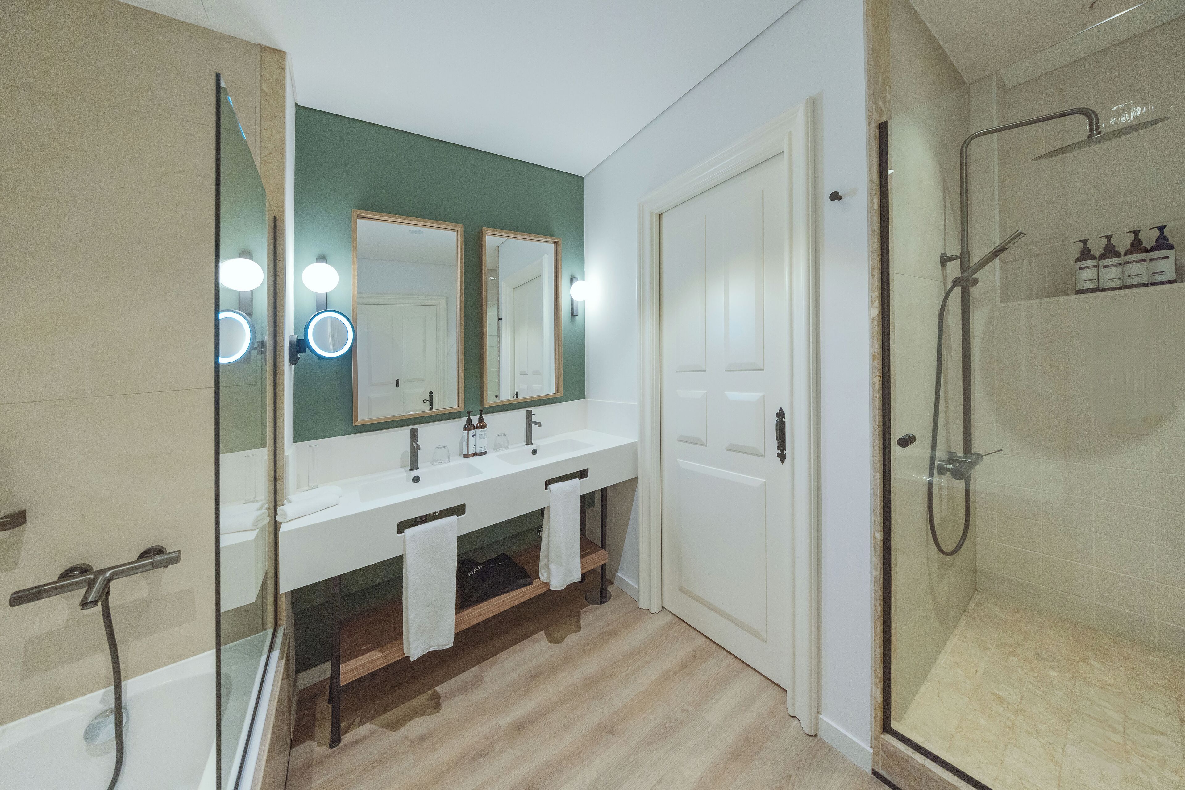A modern bathroom with a glass-enclosed shower, a white vanity with two sinks, and a large mirror with lights.