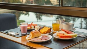 A breakfast table with plates of food, a glass of orange juice, and a cup of coffee. - Hotel Laghetto Gramado (Gramado)