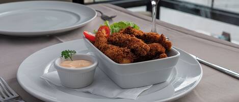 Una mesa de comedor con un plato de pollo empanizado, un recipiente pequeño con salsa y una copa de vino tinto.